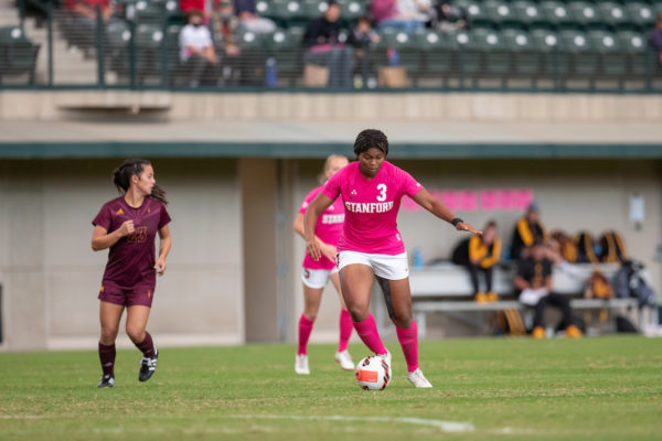 A soccer player dribbles the ball up a soccer field with two players running behind her.