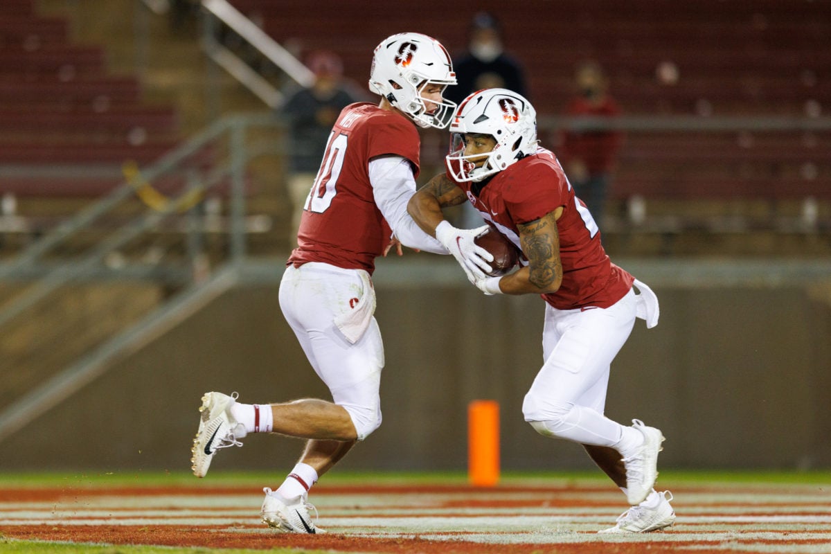 Two Stanford football players passing football to each other on the field. 