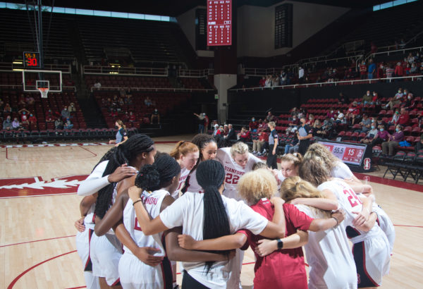 A group of Stanford basketball players huddles in a circle on the court.