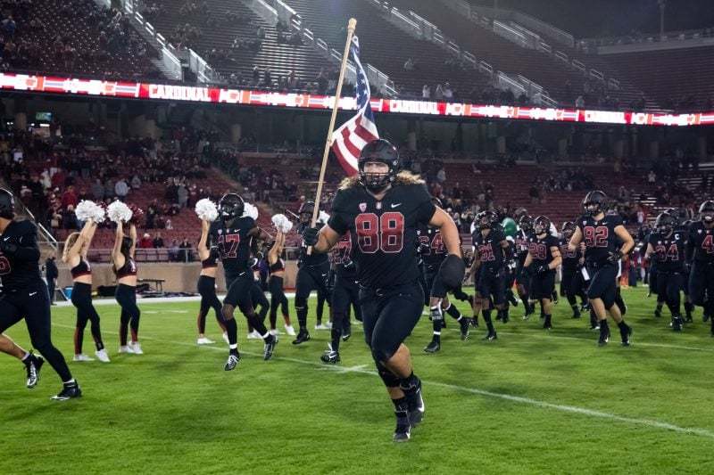 A football player runs onto the football field carrying an American flag.