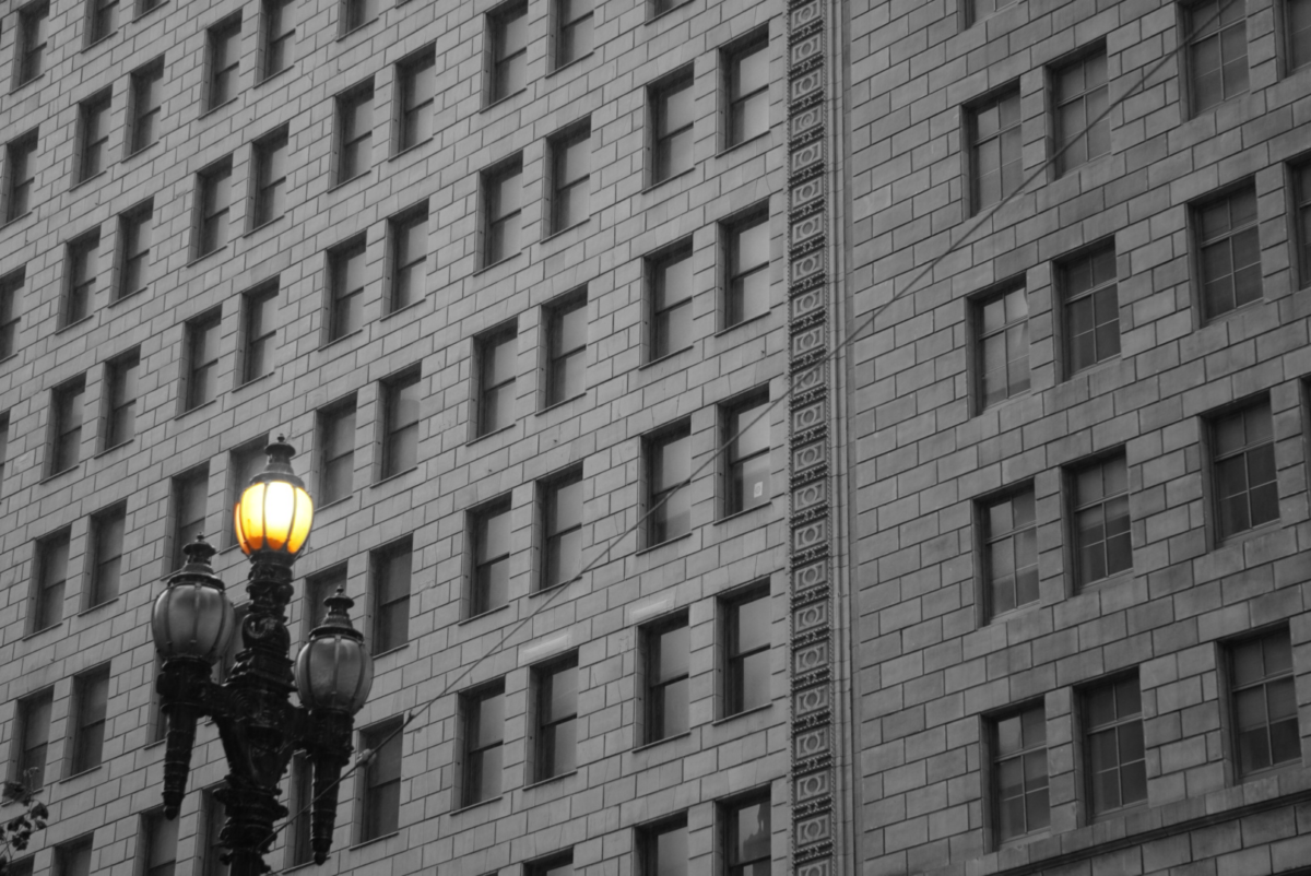 A single lamp light shines in front of the PG&E building on Harrison St. The light shines yellow while everything else is pictured grayscale.