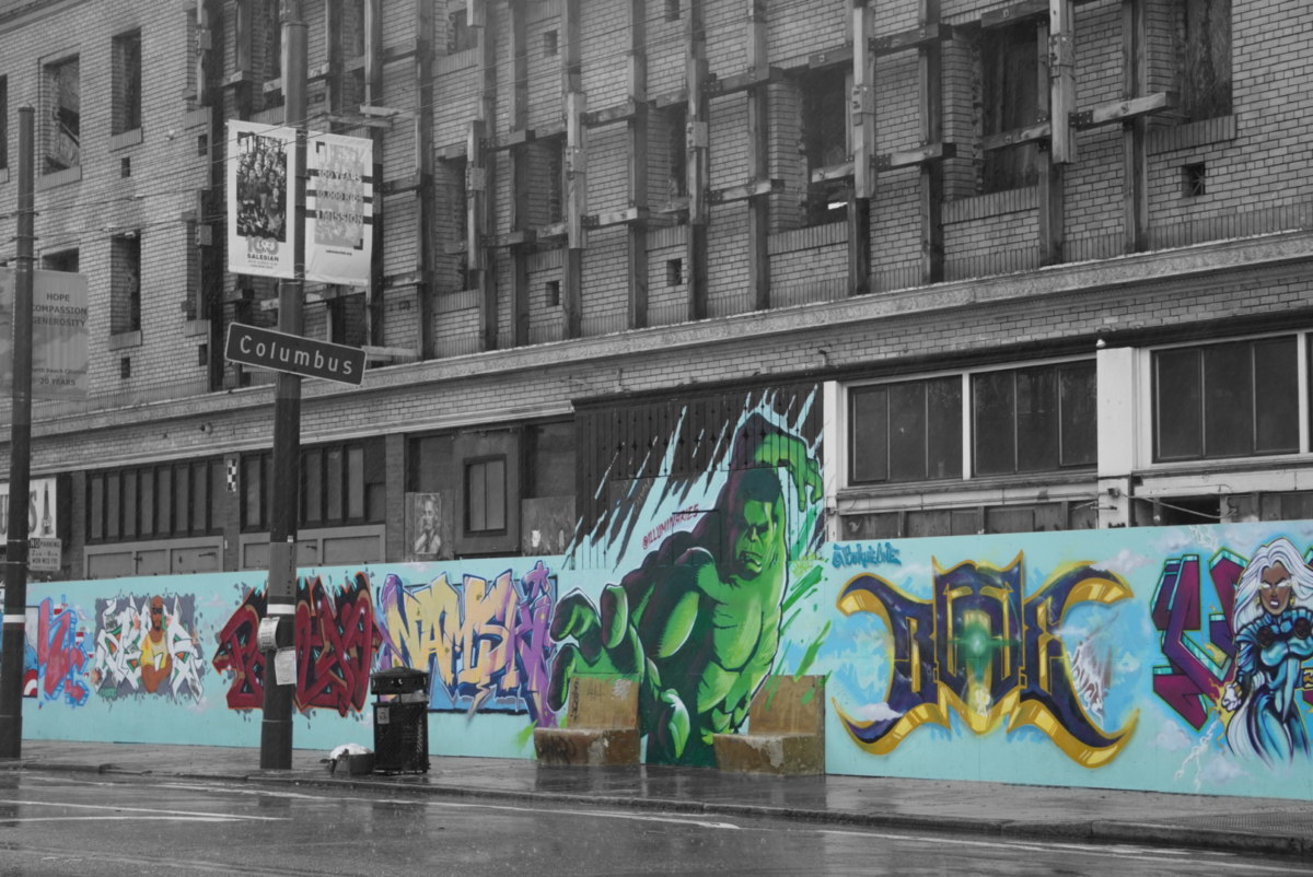 Character street art lines the walls of Columbus St. The art is colorful while the building behind it is pictured grayscale.