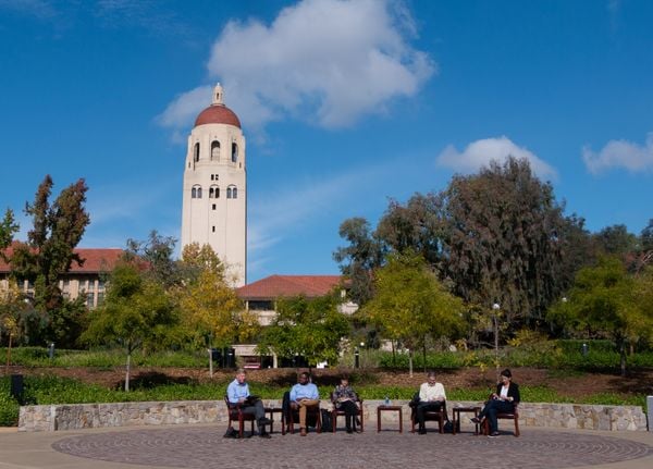 Michael McFaul, Hakeem Jefferson, Cheryl Philips, Mehran Sahami and Janine Zacharia, from left to right, sitting in chairs at Meyer Green in front of Hoover Tower.