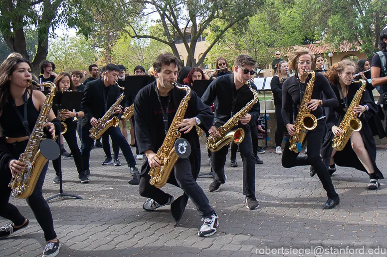 Several band members, dressed in all black, play saxophones in White Plaza.