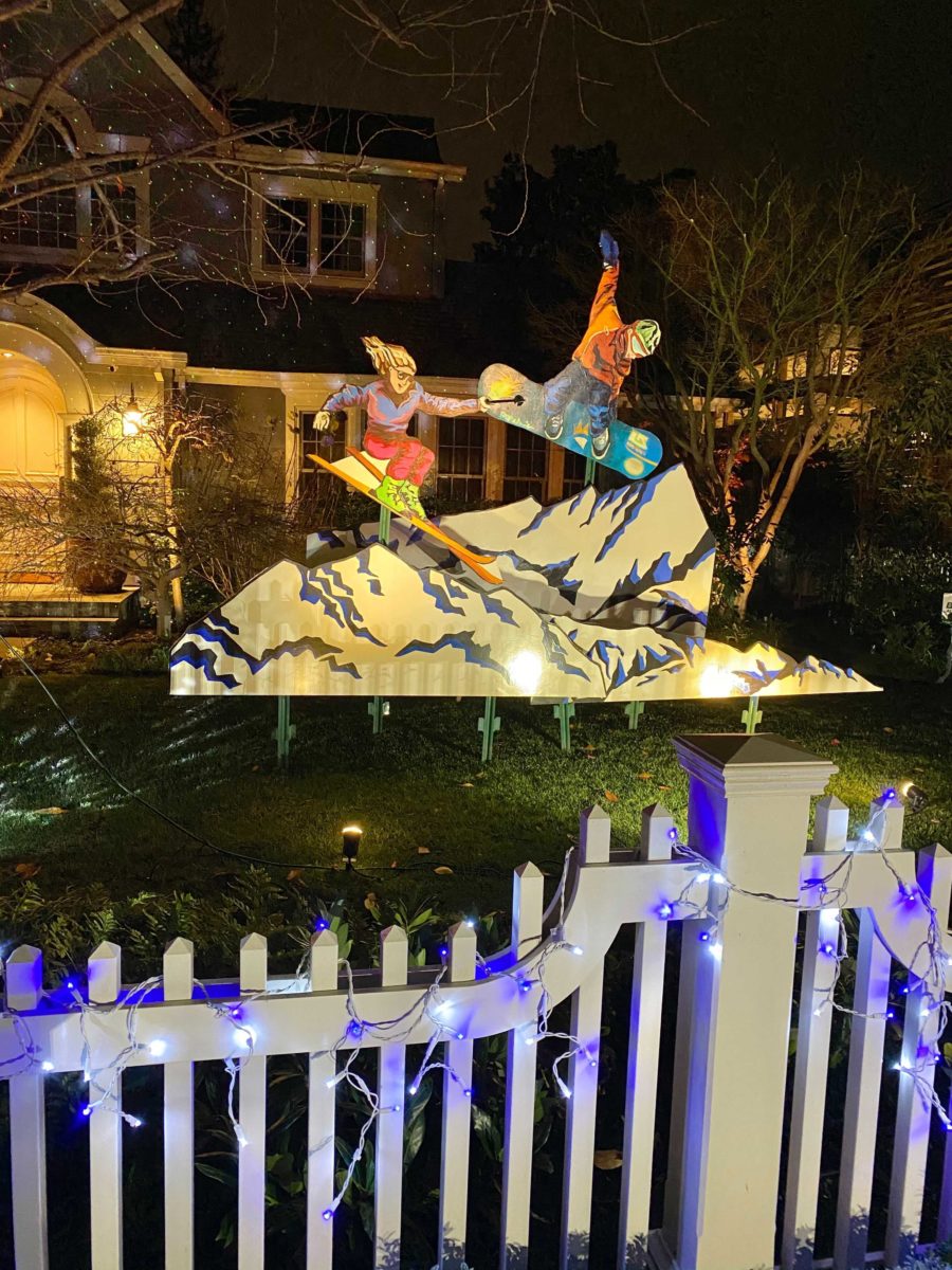 An outdoor holiday decoration display showing a skier and snowboarder atop a mountain. 