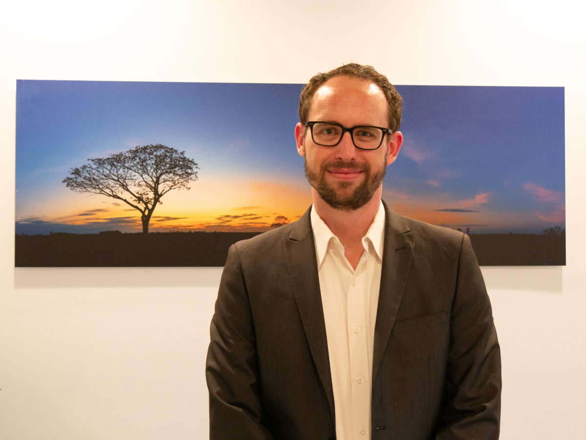 David Carreon stands in front of a wall painting of an Acacia tree