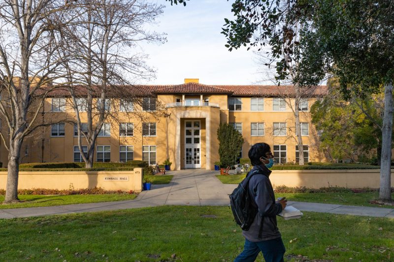 A masked student walks in front of Kimball Hall, an undergraduate residence.