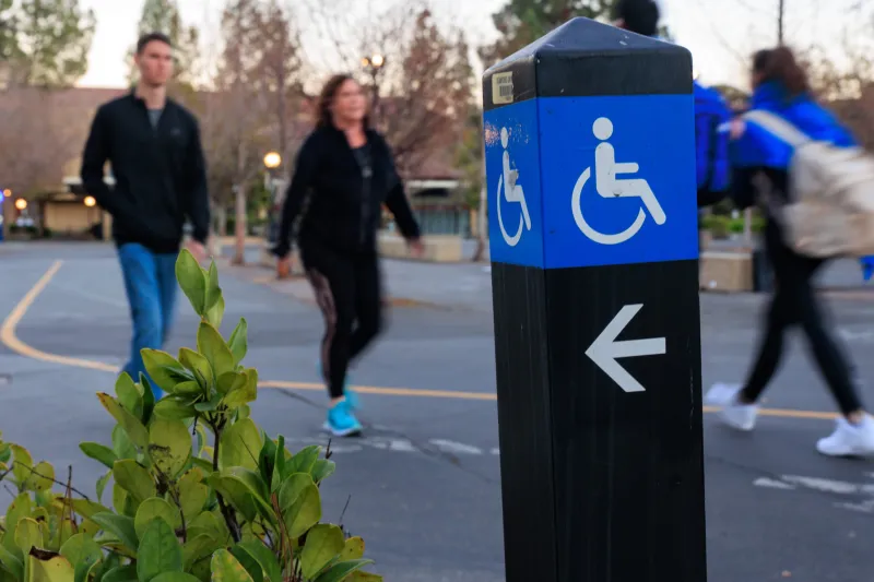 Bikers and pedestrians pass a disability placard at Stanford University’s White Plaza
