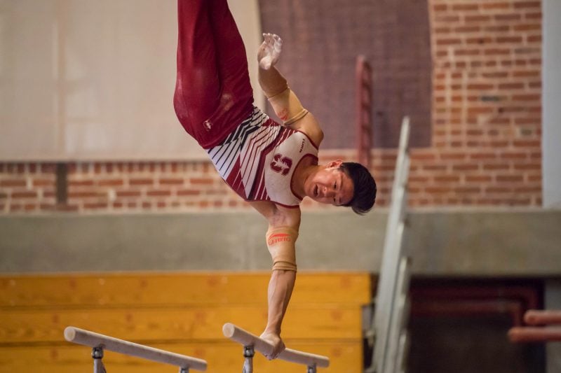 A gymnast flips upside down on one arm on the parallel bars.