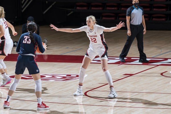 A women's basketball player stands on the court with her arms extended, playing defense