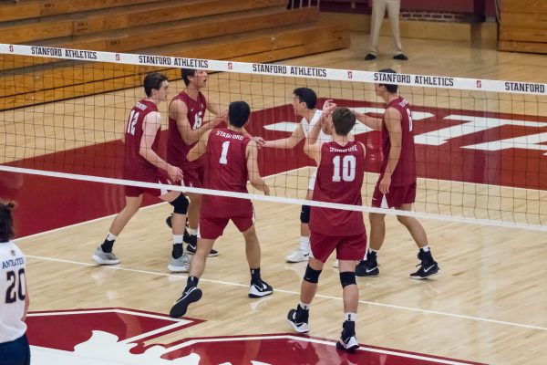 Six Stanford men's volleyball players celebrate a play behind the volleyball net.