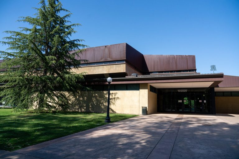 Maples Pavilion from the southwest side of the building, with a pine tree in front.