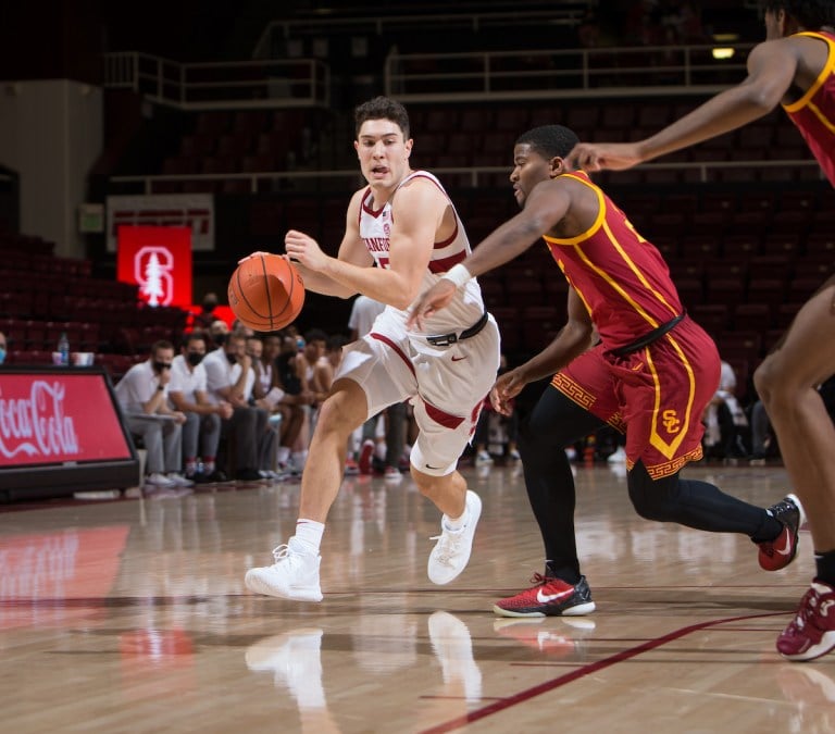 A basketball player drives to the basket with another player playing defense from behind.