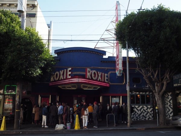 A crowd of people standing in front of a theater with the word "Roxie" written on the facade.