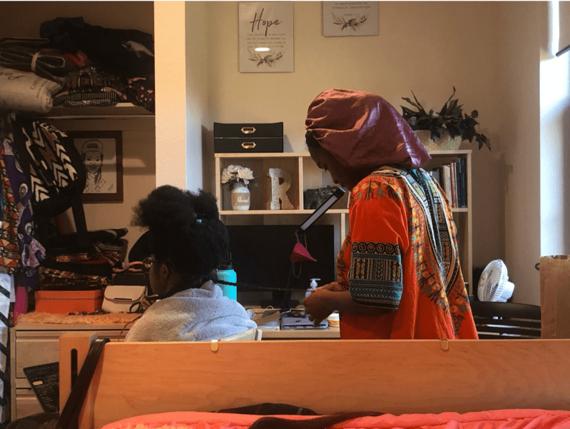 A woman braids another woman's hair