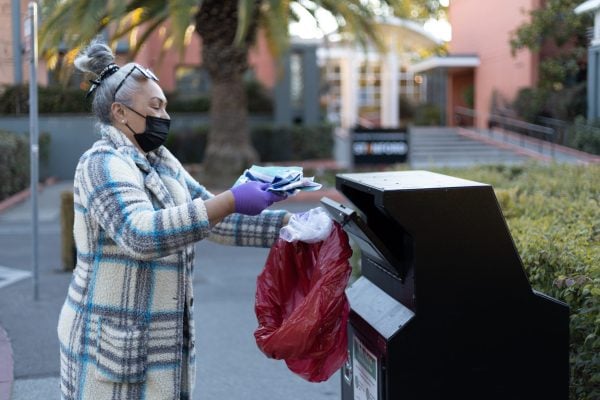 Woman wearing gloves dropping off a bag of COVID tests at the metal drop box
