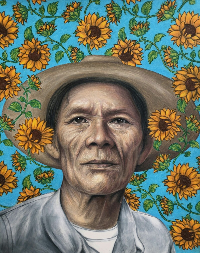 A man, surrounded by sunflowers, looks directly into the camera.