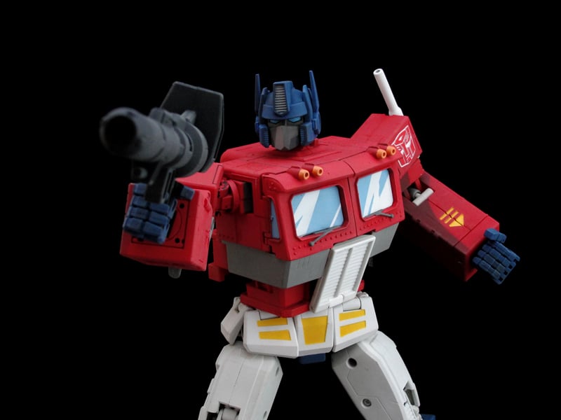Toy robot of transformer Optimus prime, who is posing with a toy gun that is pointed in front of him