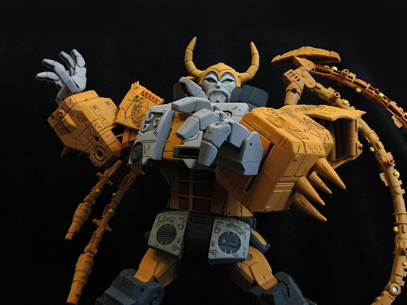 Toy robot of transformer Unicron, a yellow bot with wing like parts who appears to be reaching out to the audience