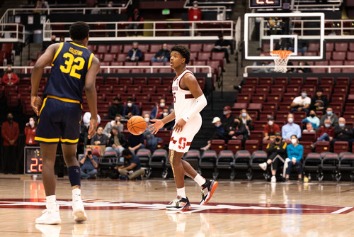 A basketball player dribbles the ball down the court with a player defending him.