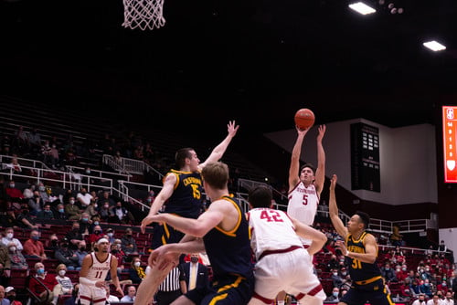 Two basketball players fight for position as another player in the background shoots the ball.