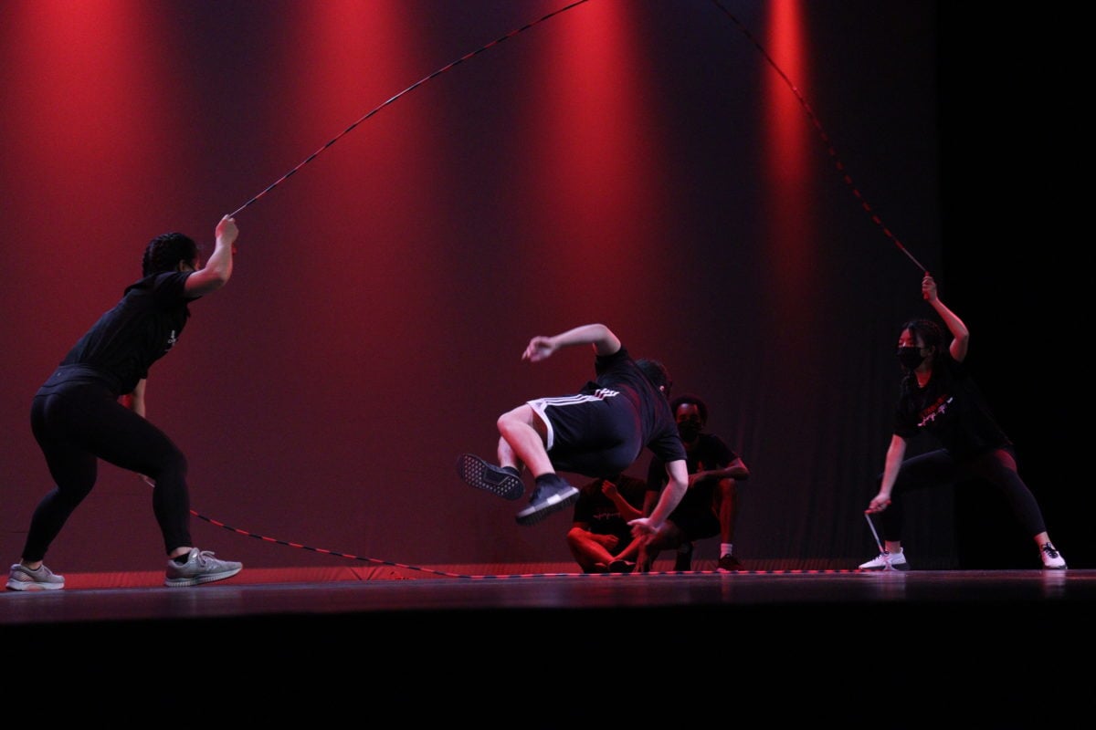 Two people hold jump ropes while one person dances in the center.