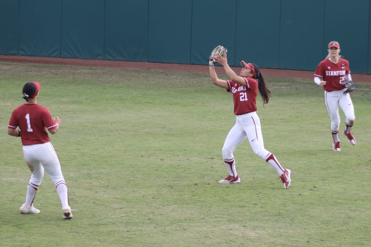 Three players are in the outfield, with two watching as one waits to catch a ball.