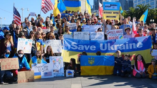 A group of protestors holding signs and Ukrainian flags gather for a photo at the 'Stand With Ukraine' rally