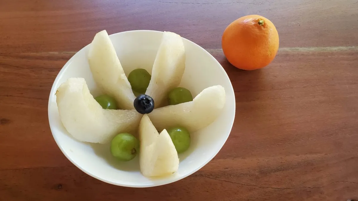 A plate of sliced pears arranged into flower, green grapes between each and a blueberry at the cent. A whole tangerine sits next to the plate.