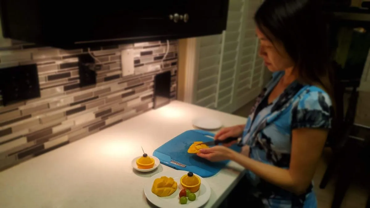 A woman (the author's mom) slices a mango above a counter and cutting board. To the left are two plates of fruit.