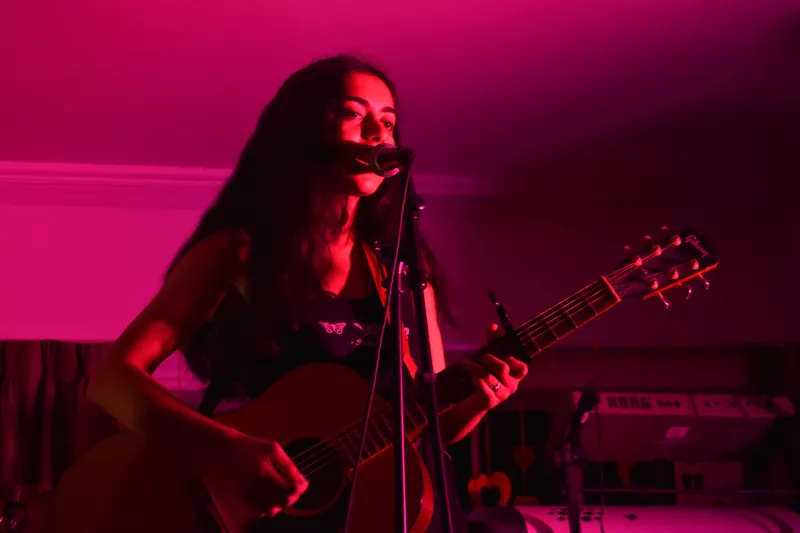 Woman plays guitar and sings with pink lighting
