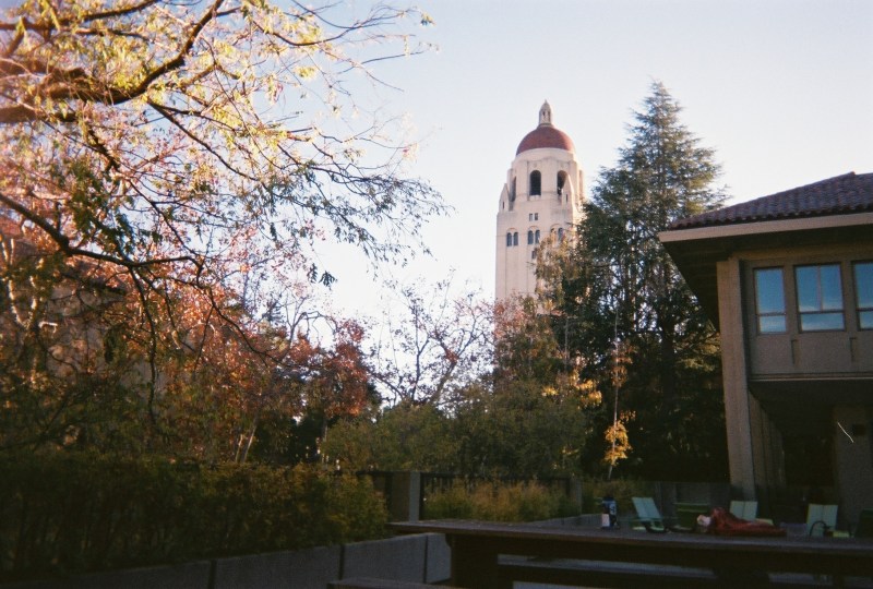Hoover Tower stands in the distance behind a shaded picnic table and grove of trees.