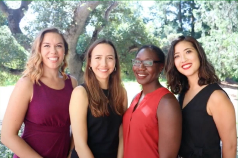 Four women stand together and smile at the camera.