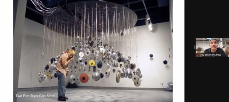 A Zoom screenshot of artist Terry Berlier on the right hand-side and the sculpture of suspended pan tops that are paired together perfectly.