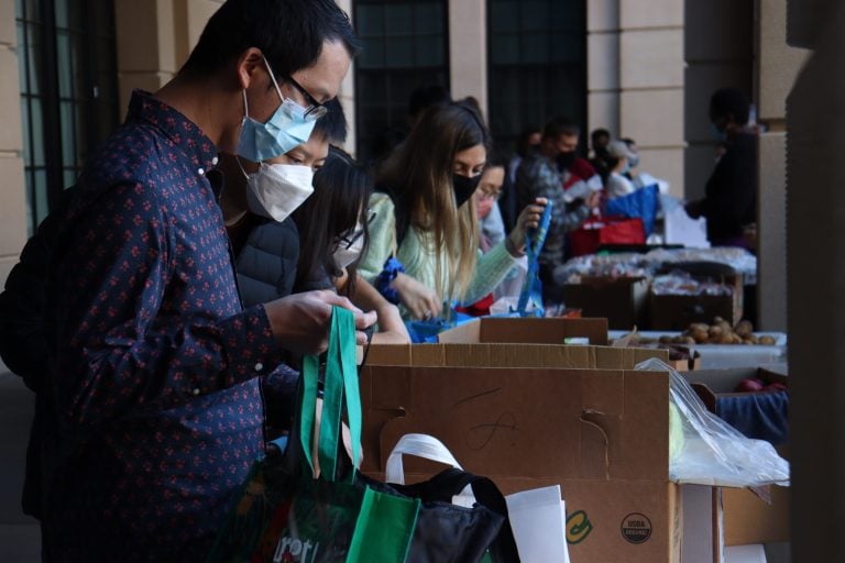 Side view of pantry-goers looking at produce on tables with reusable bags.