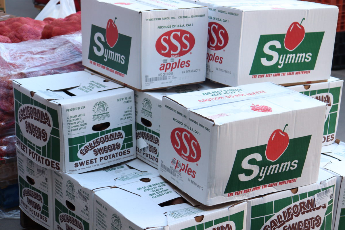 Stack of about 12 white boxes of produce with "Symms apples' and "California Sweet Potatoes" written on the boxes 