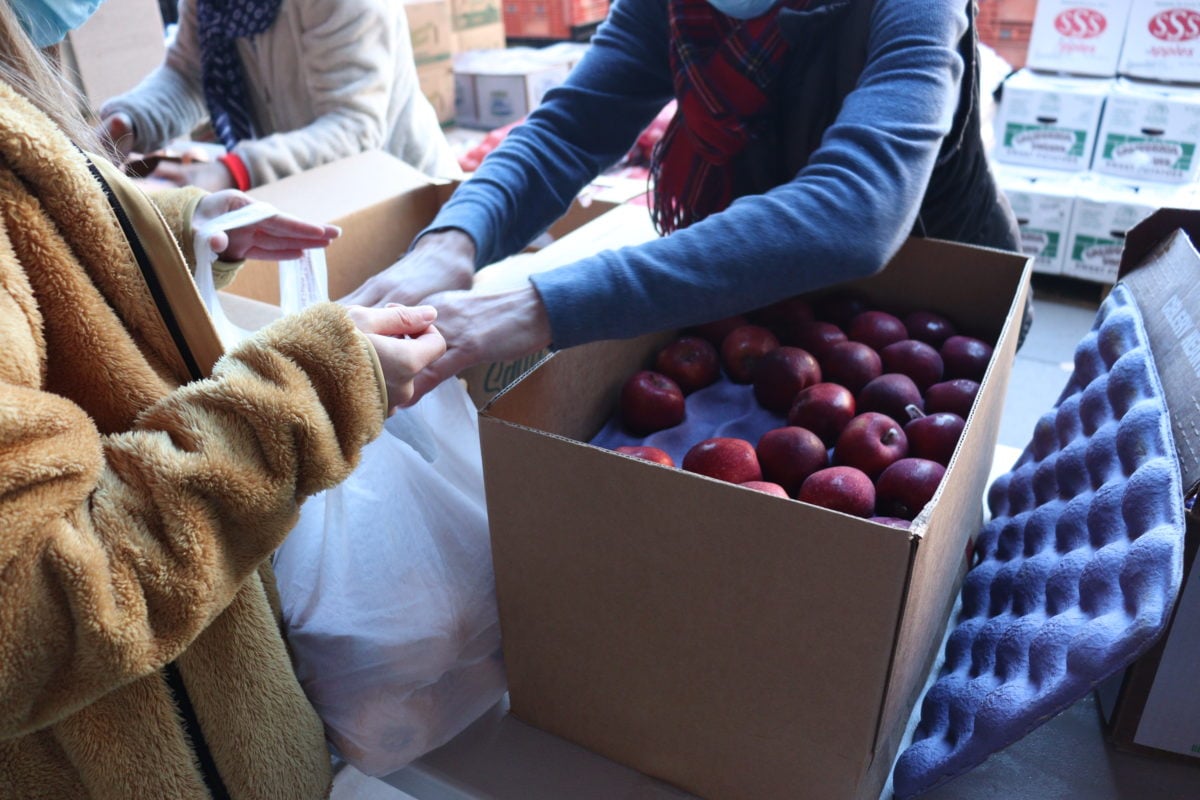 Volunteer loads a student’s bag with apples from a box of apples. 