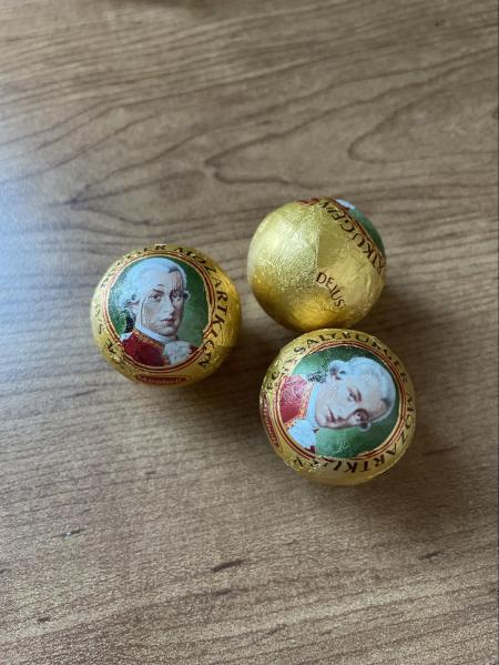 Three foil-wrapped Austrian chocolates with a portrait of Mozart on them sit on a wooden table