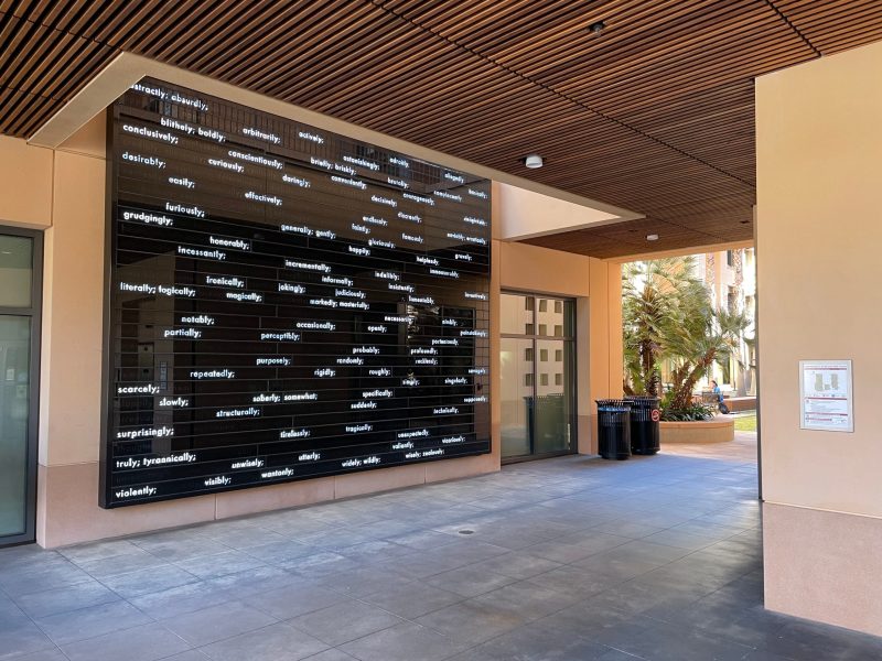 A reflective, dark wall at the Stanford Graduate School of Business, containing various English adverbs sporadically lit up all over