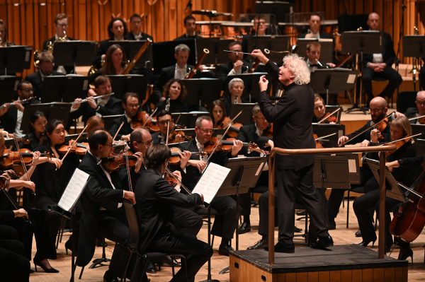 Simon Rattle waves the baton at the podium, conducting the London Symphony Orchestra