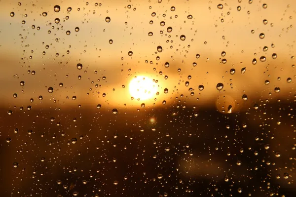 the blurred view of the sun through a window wet from rain