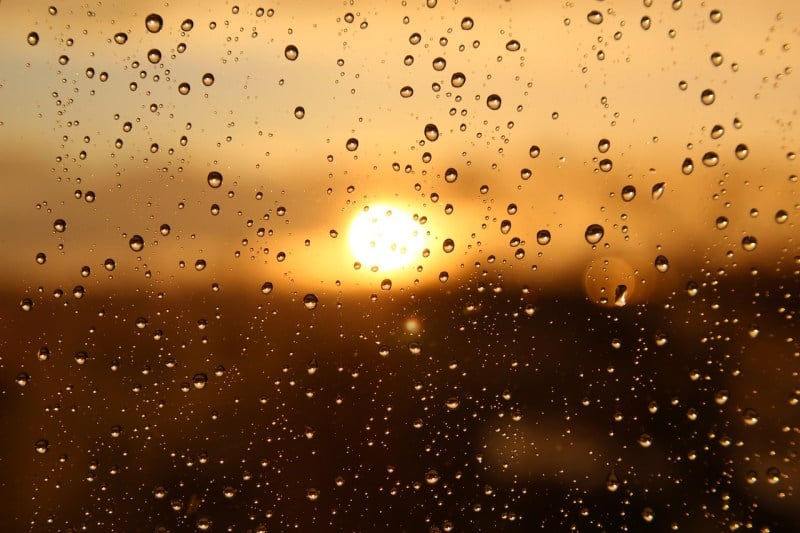 the blurred view of the sun through a window wet from rain