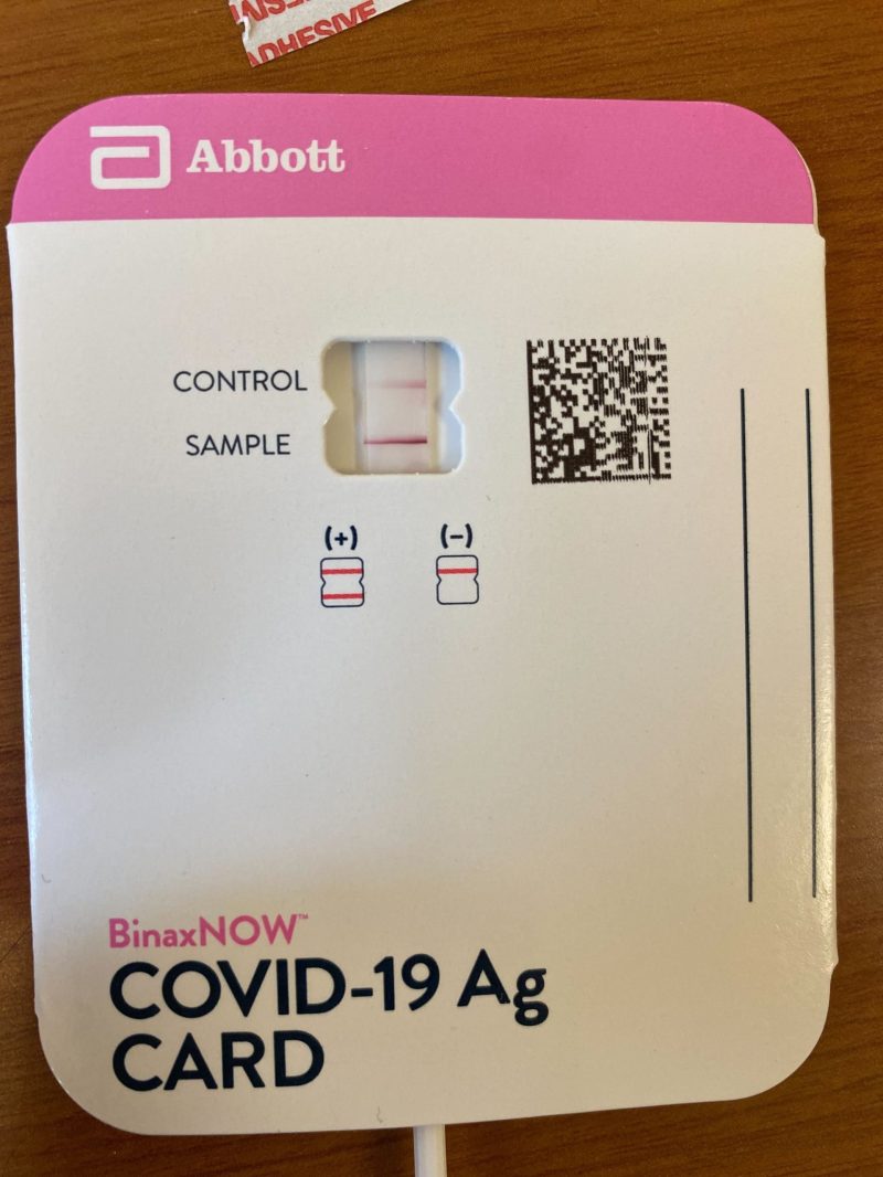 Pink and white COVID-19 rapid test, displaying two lines that signify a positive test.