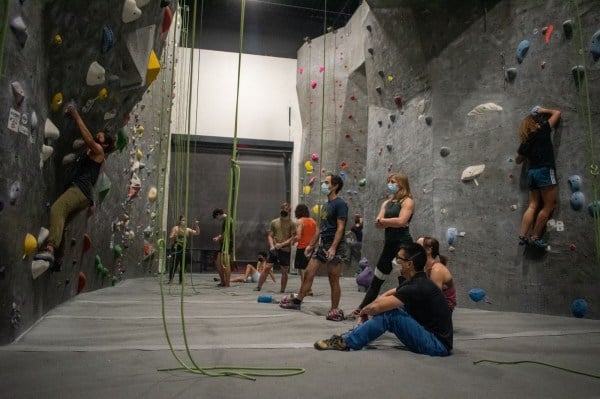 A group of rock climbers watch their teammate scale a climbing wall