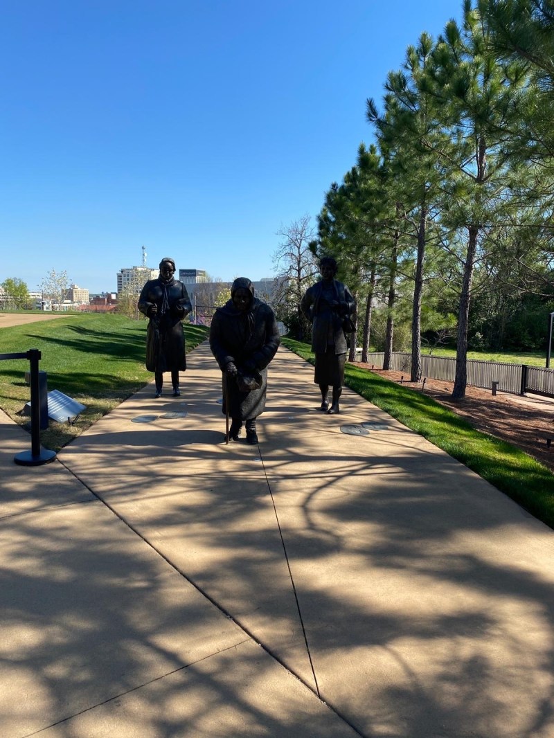Statues of Black women civil rights leaders at the Equal Justice Initiative’s Legacy Museum. Three statues of women stand on a outdoors walkway by a row of trees.