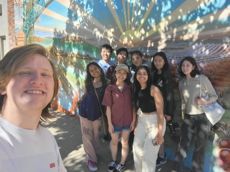 A group of students smile in front of a mural in Modesto.