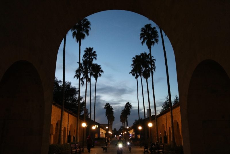 The silhouette of an archway frames the silhouettes of palm trees at Stanford.