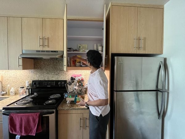 A man stands with his back turned to the camera, pulling something out of his kitchen drawers.