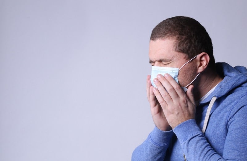 Man with mask coughing and touching his mouth over his mask with his hands