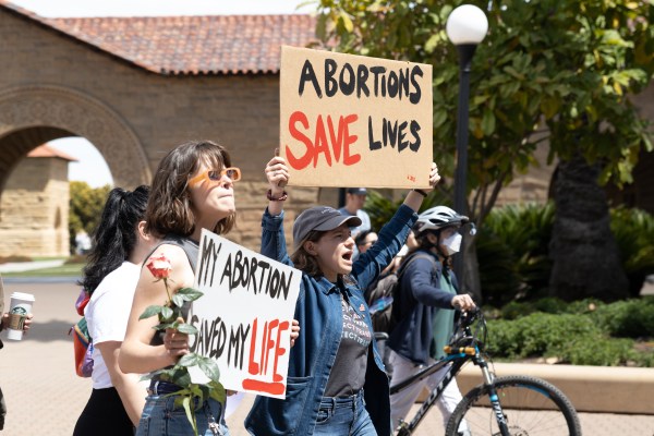 People hold signs that say "ABORTIONS SAVE LIVES" and "MY ABORTION SAVED MY LIFE" in Main Quad